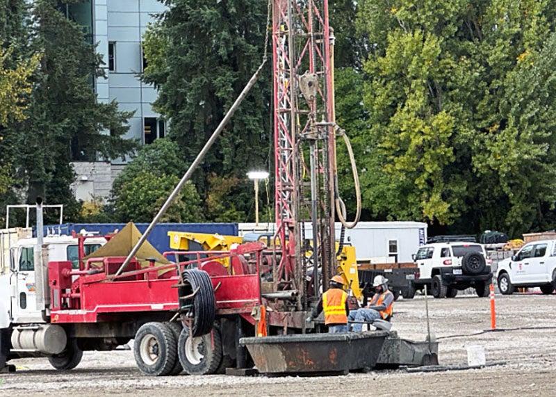 a tall metal structure is attached to the back of a truck with part of it in the ground. two workers are next to it.