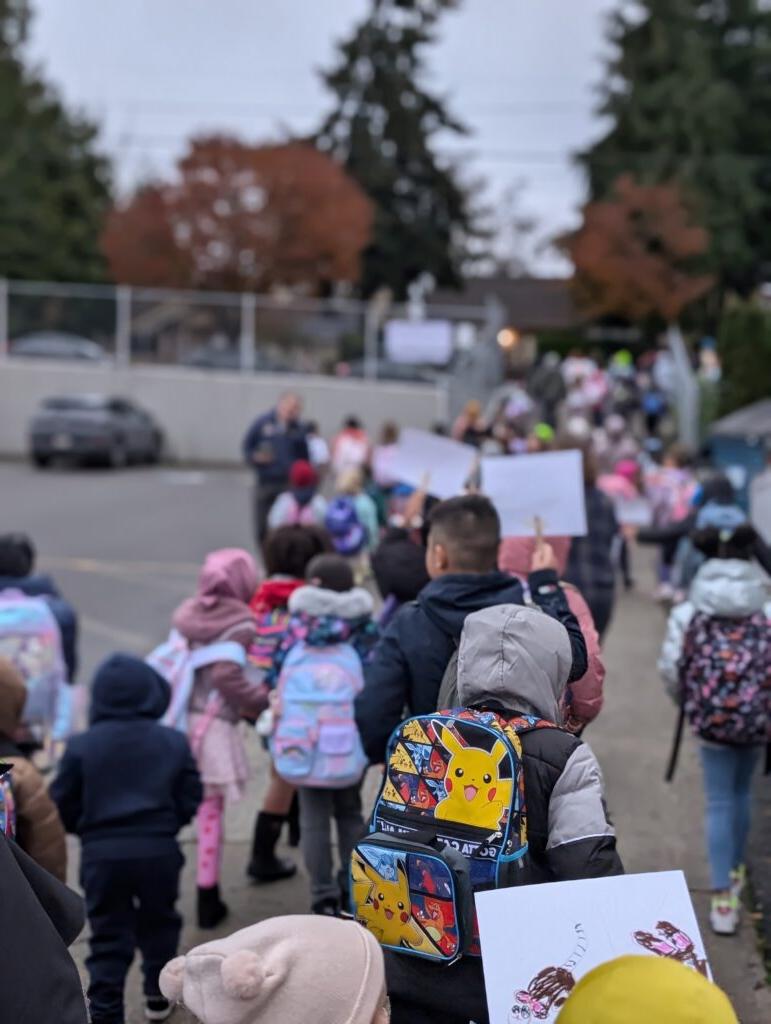 Students hold signs and walk in group to school entrance.